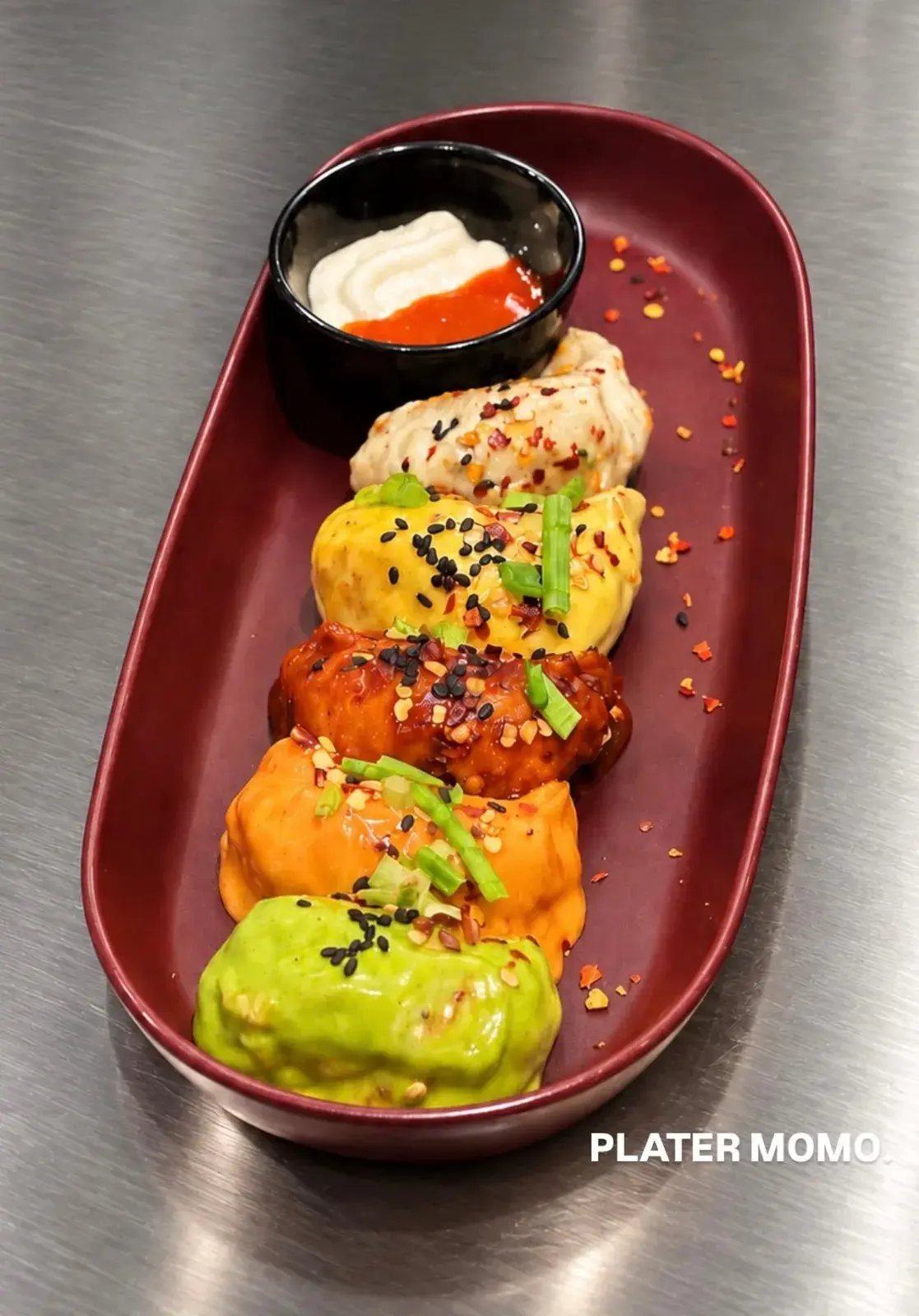 A platter of colourful momos with a dip on a red plate