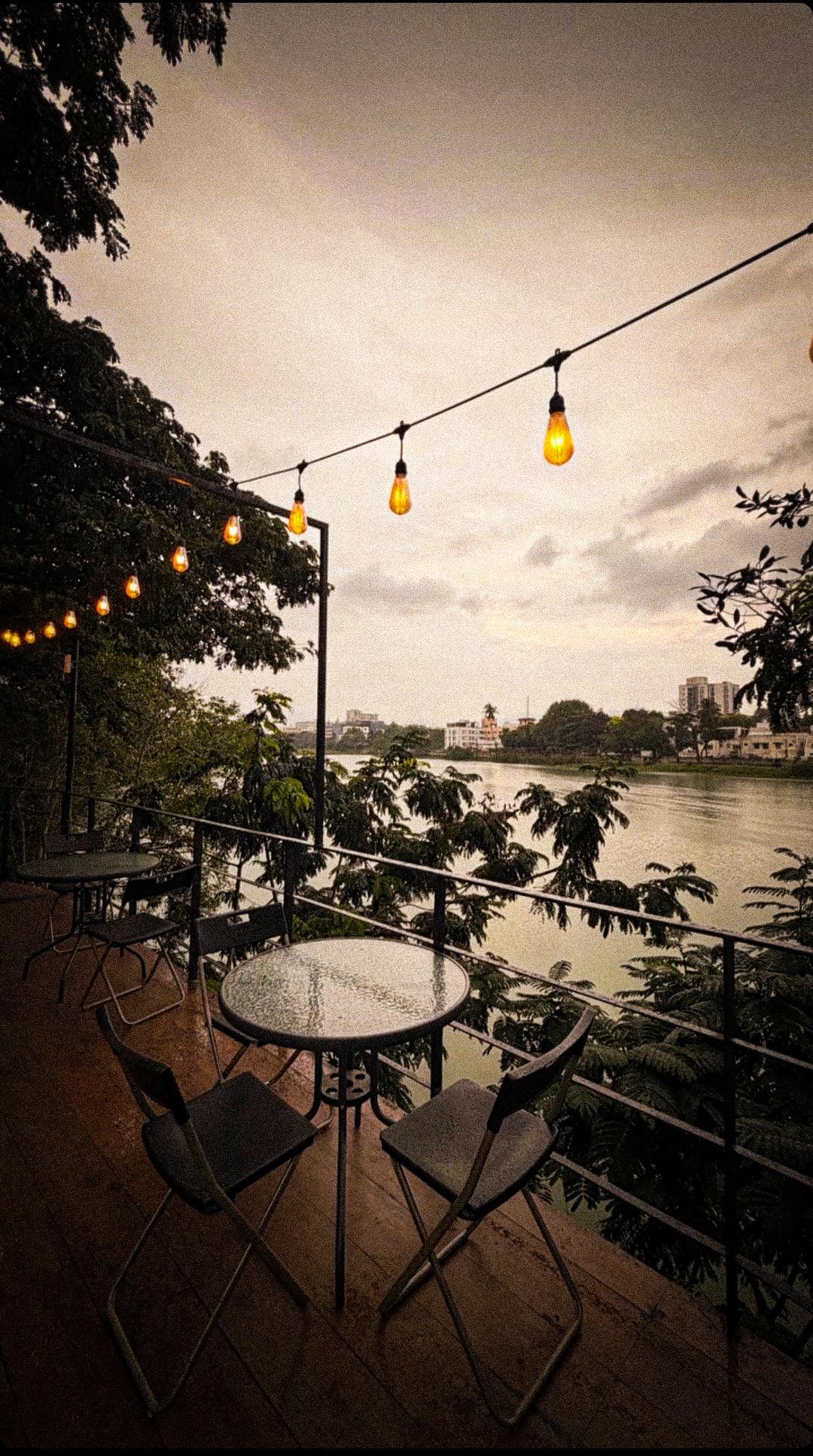 A glass-topped table on the wooden deck under glowing string lights, the lake and city beyond at dusk